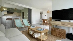 A modern living room with a sofa, a coffee table with books, a TV, and a dining area with chairs. - Holiday Home in Terenez with Sea Views (Plougasnou)