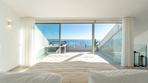 Un dormitorio con una cama grande, un escritorio y vistas al mar a través de ventanales del suelo al techo.