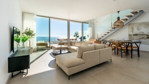 Una sala de estar moderna con un sofá grande, una mesa de comedor con sillas y una escalera que sube a un nivel superior.