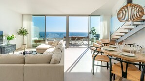 Una sala de estar moderna con un sofá grande, una mesa de comedor preparada para cuatro personas y una escalera que sube a un piso superior.