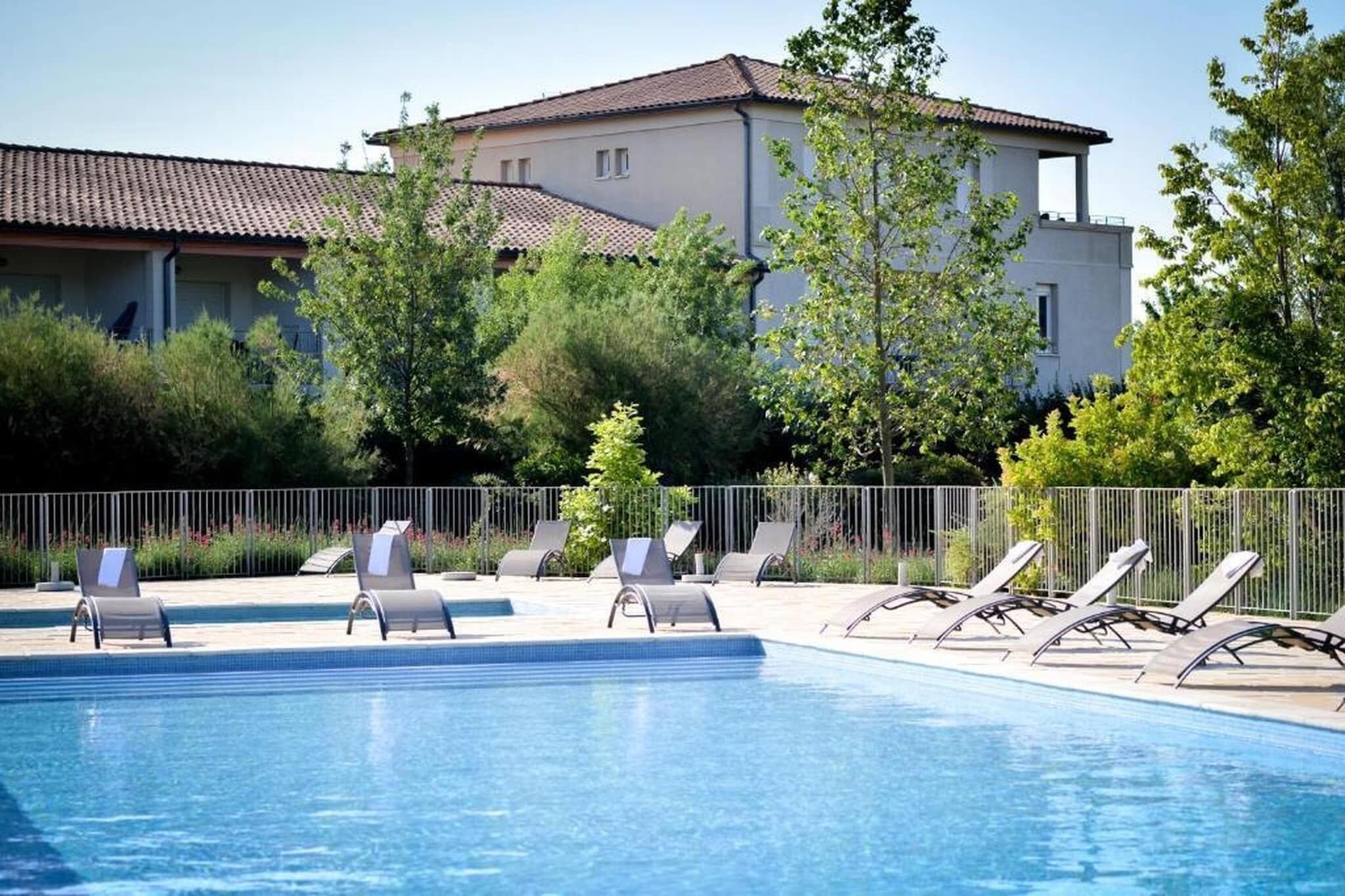 Uma piscina com espreguiçadeiras, uma cerca e um edifício ao fundo.