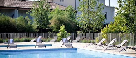 A swimming pool with lounge chairs, a fence, and a building in the background.