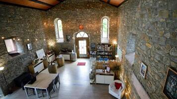 A rustic interior with stone walls, a wooden ceiling, a dining area with a table and chairs, a bar area with bottles, and a fireplace.