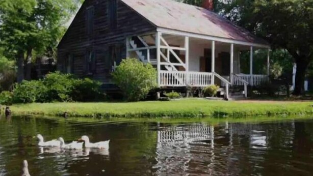 Ein rustikales Holzhaus mit Veranda und Teich mit Enten.