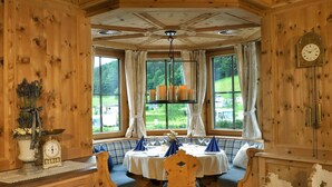 A wooden interior with a dining table set for two, a clock on the wall, and a window with curtains. - Chalet near Beach & Nature in Austria (Kramsach)