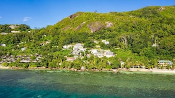 A coastal resort with multiple buildings nestled among lush greenery, overlooking clear turquoise waters.