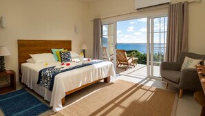 Une chambre avec un lit, une chaise, un canapé, un balcon donnant sur la mer et un appareil de climatisation.