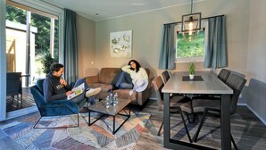 A modern living room with a sofa, coffee table, and dining table. There is a large window with curtains, a hanging light fixture, and a wall-mounted artwork. - Chalet in Tyrol near Ski Slopes (Kramsach)