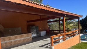 Un espacio al aire libre techado con una parrilla, una piscina y un área de estar con sillas.