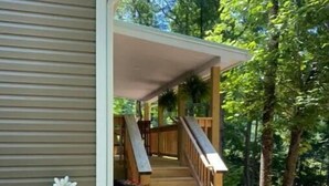 A wooden staircase leading to a covered porch with a railing, surrounded by greenery and a gravel path. - Mountain Hideaway - HOT TUB (Horse Shoe)