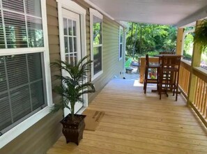 A wooden deck with a potted plant, a wooden table and chairs, and a view of greenery.