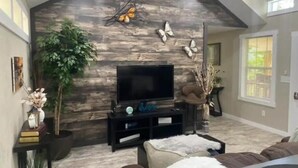 A modern living room with a stone wall, a flat-screen TV, and a large plant. - Mountain Hideaway - HOT TUB (Horse Shoe)