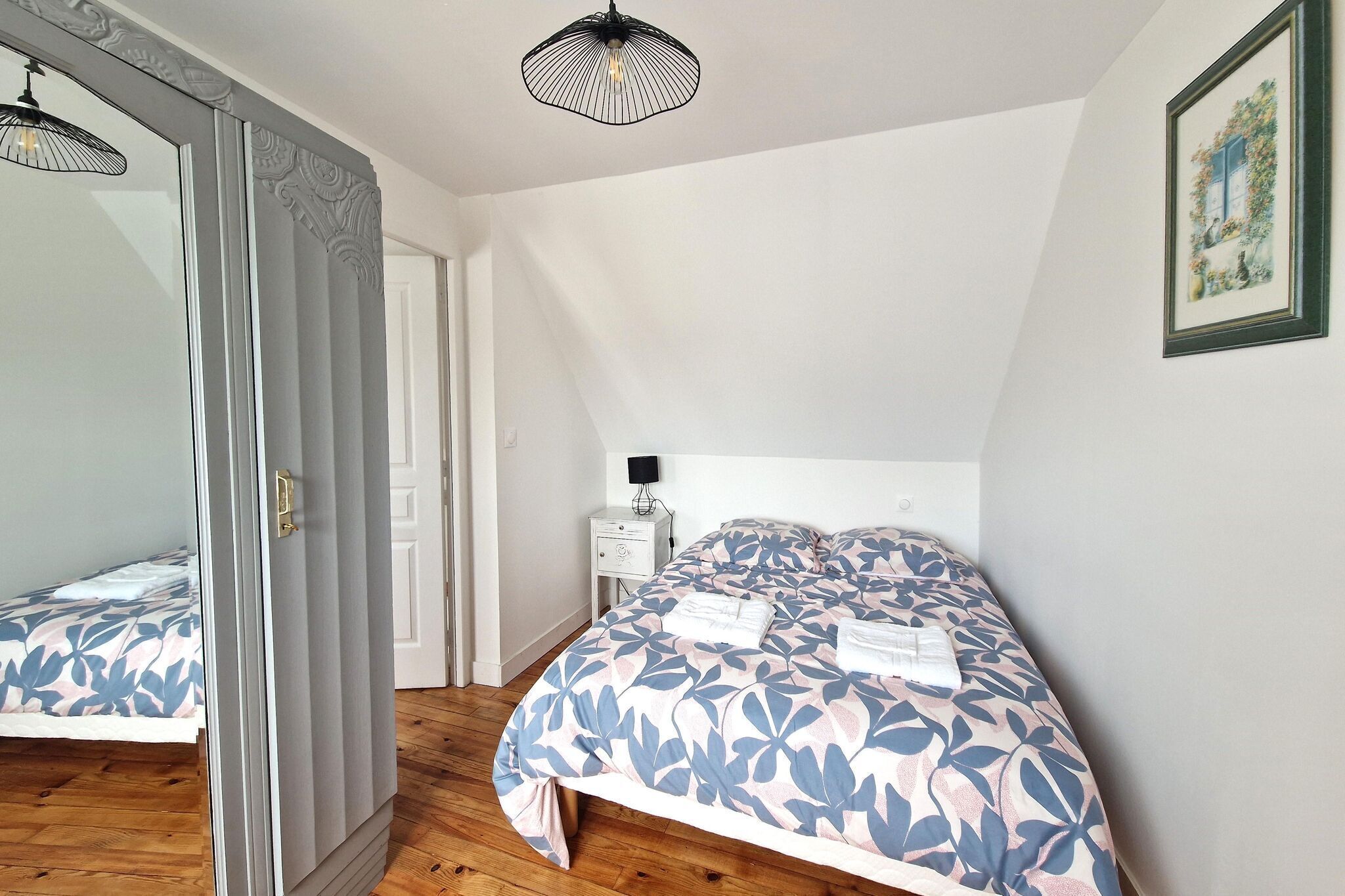 A bedroom with a large bed, a bedside table with a lamp, and a mirror.