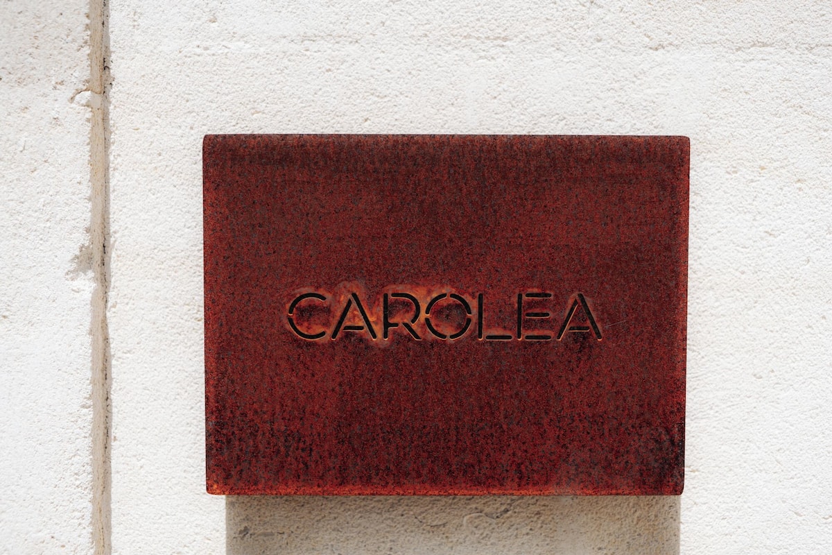 Eine rote Plakette mit dem eingravierten Wort 'CAROLEA' an einer weißen Wand.