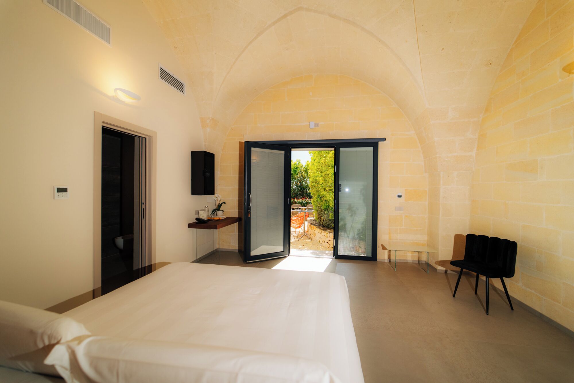 Ein Schlafzimmer mit Bett, Bad, einer kleinen Sitzecke und Blick ins Freie.
