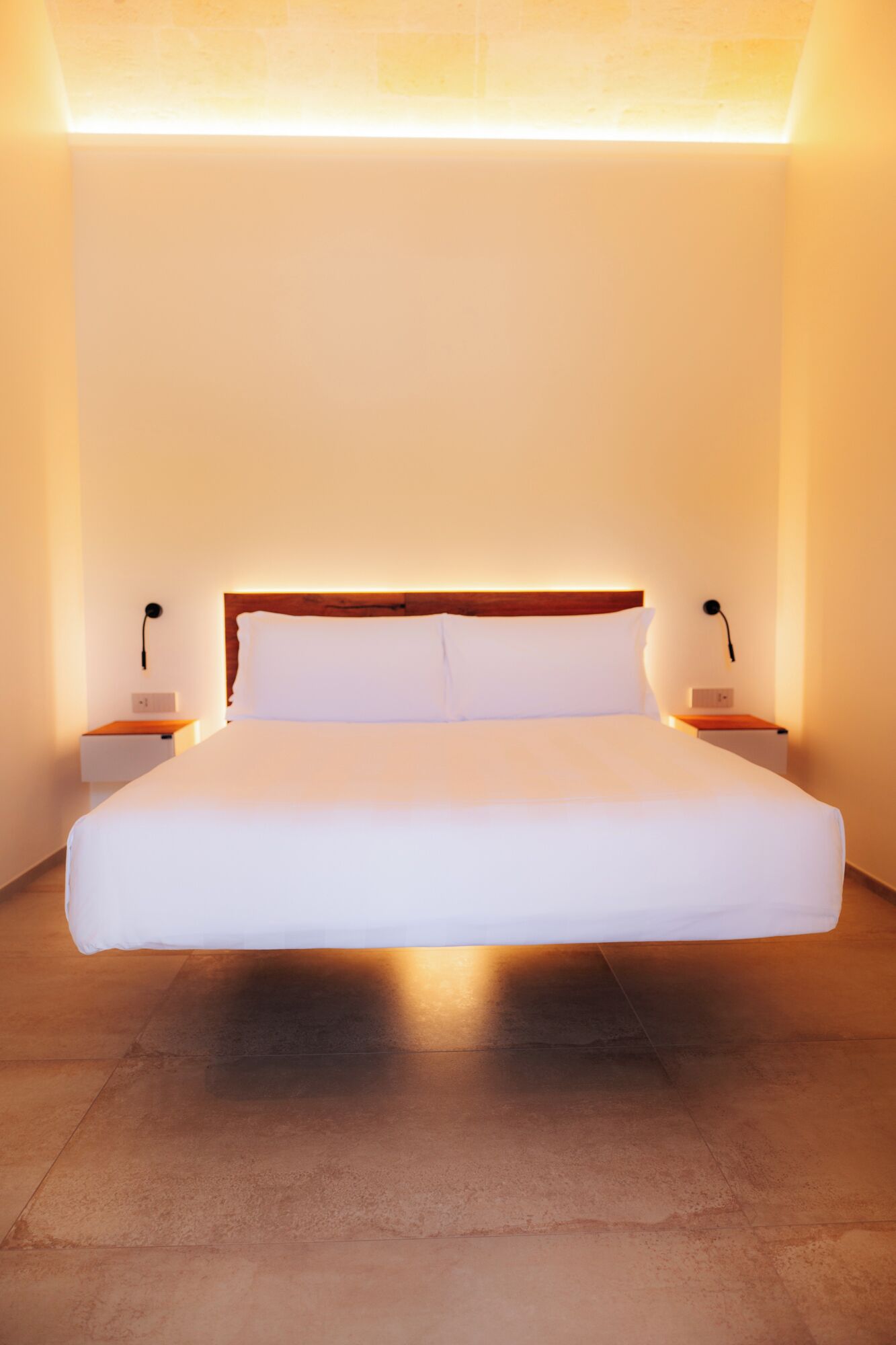 A large bed with white linens in a room with a wooden headboard, two bedside tables, and a light fixture above the bed.