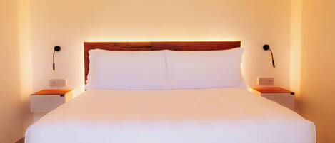 A large bed with white linens in a room with a wooden headboard, two bedside tables, and a light fixture above the bed.