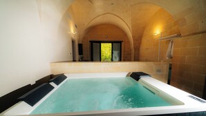 Ein Wellnessbereich mit einer großen Whirlwanne, einer gewölbten Decke und Blick auf eine grüne Außenanlage.