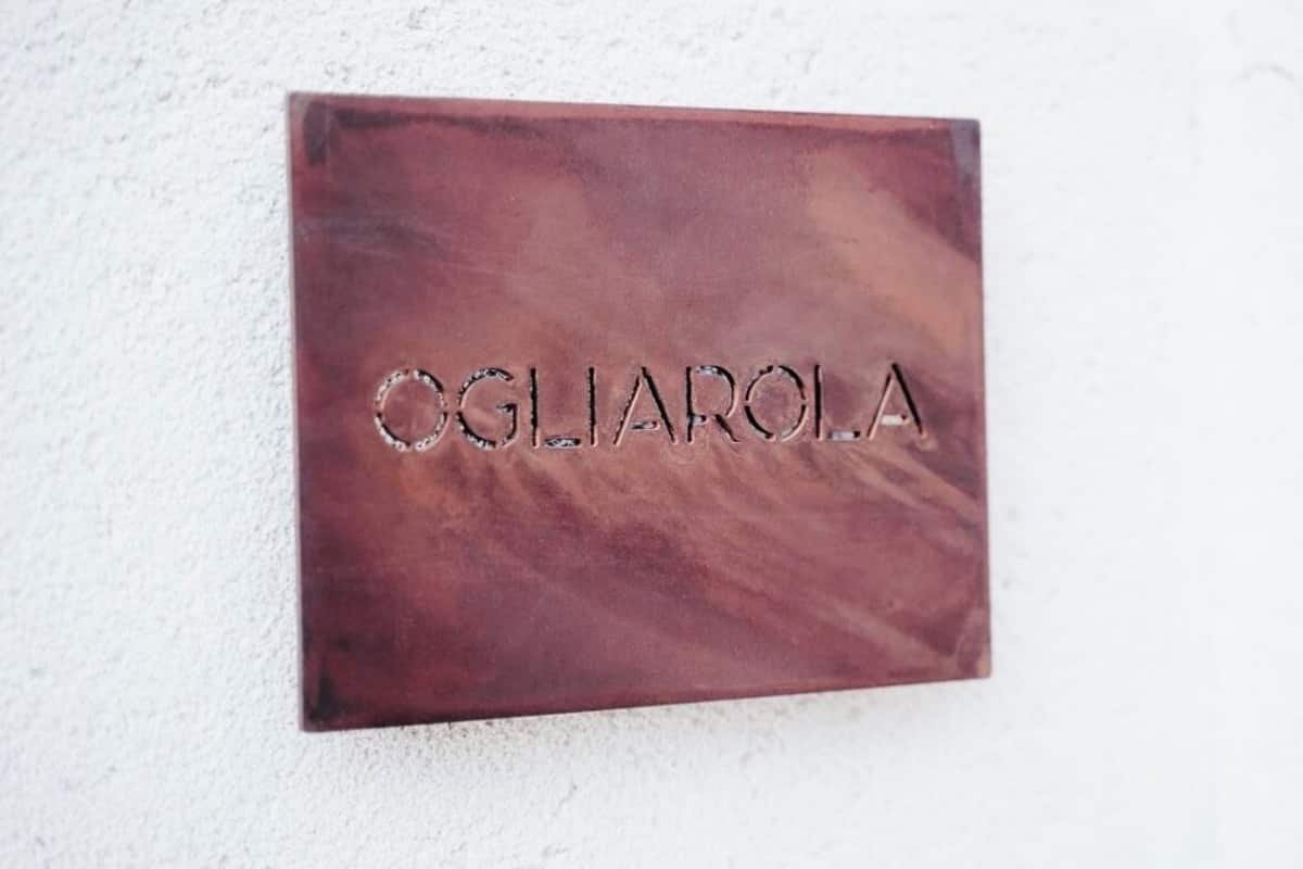 Eine rechteckige Plakette mit der Aufschrift 'OGLIAROLA', angebracht an einer strukturierten Wand.