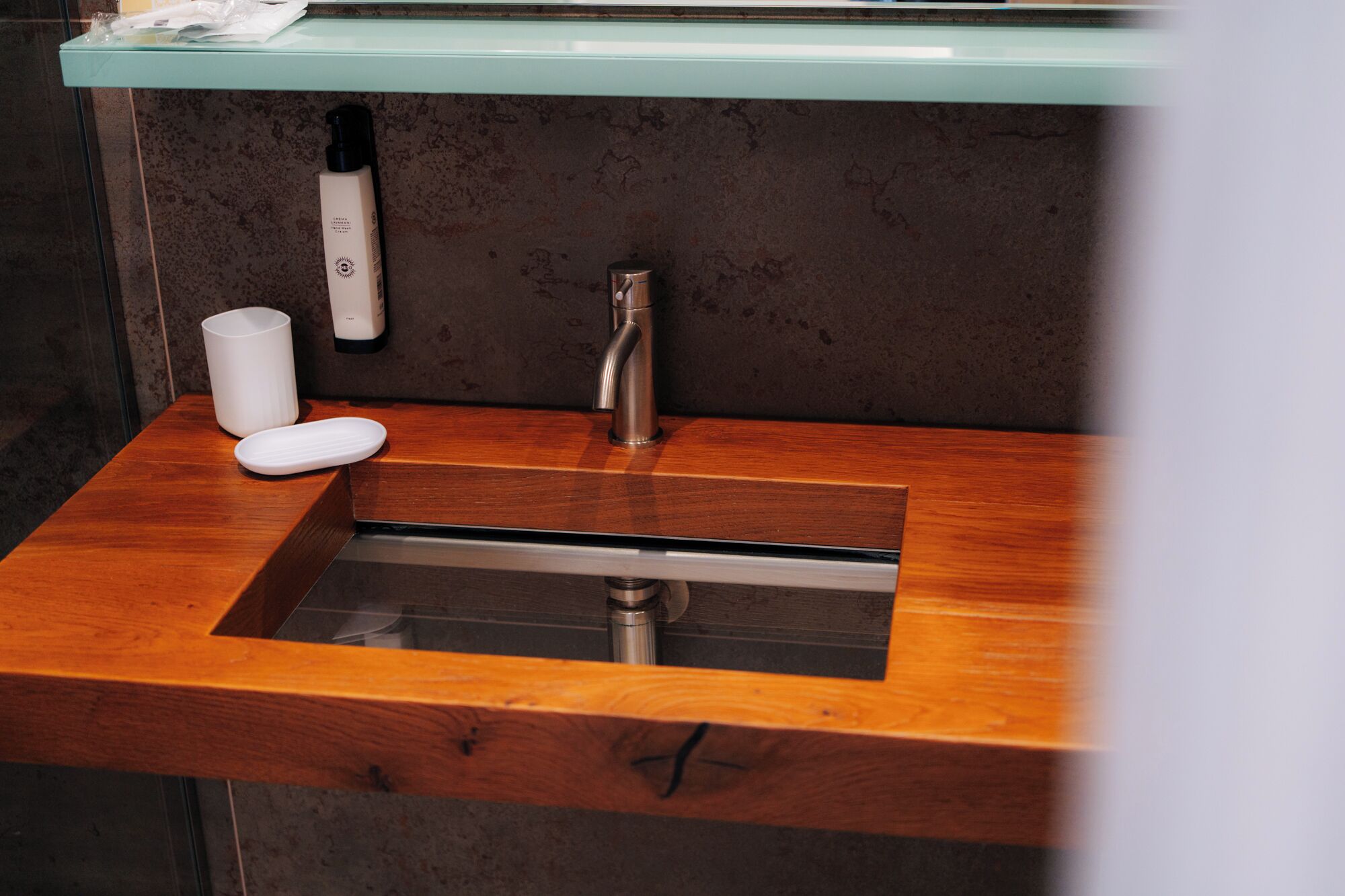 A bathroom with a wooden vanity, a sink, a faucet, and a soap dispenser.