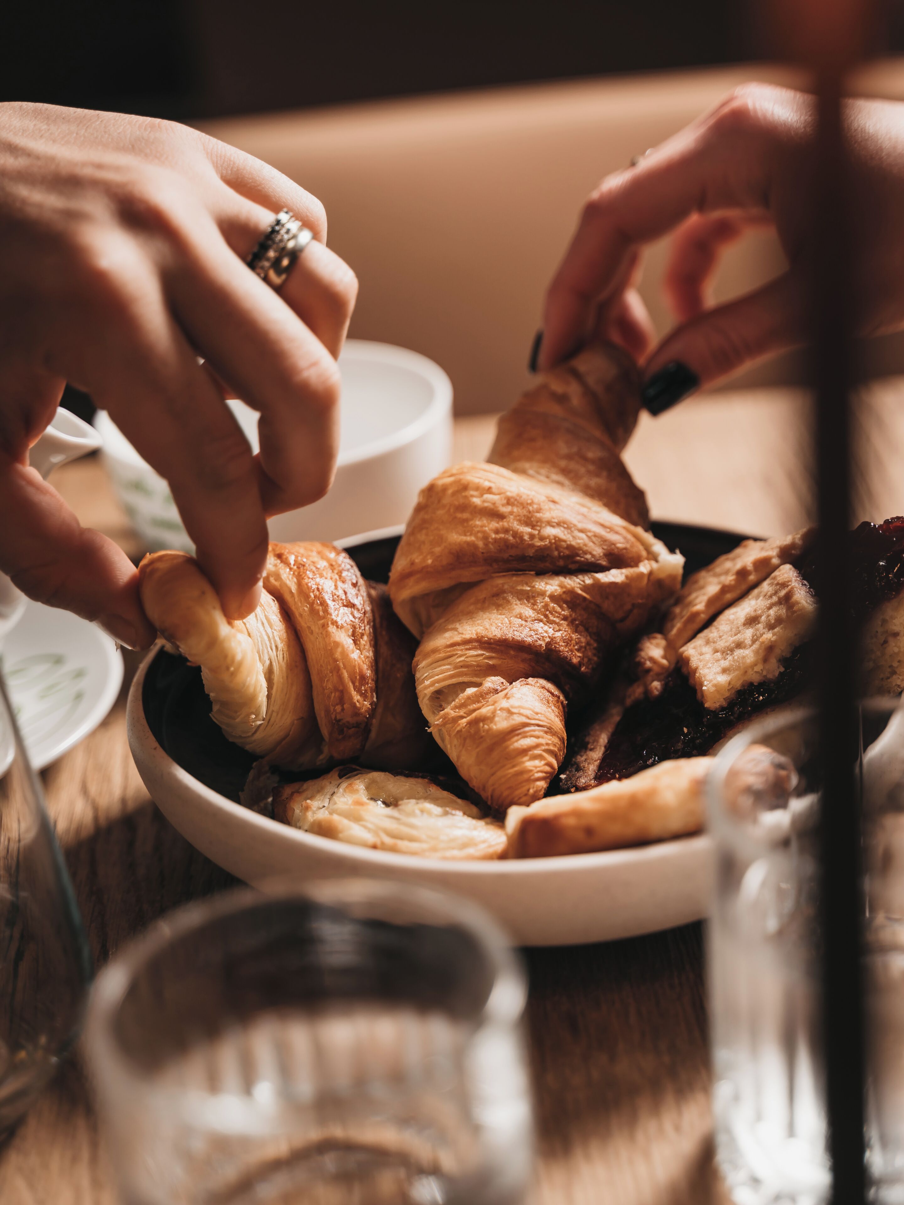 Eine Schale Croissants auf einem Tisch, dazu ein Glas Wasser und eine Tasse.