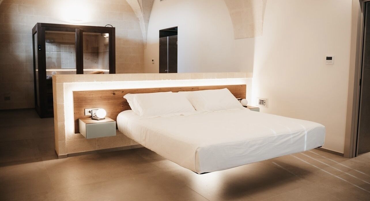 Un dormitorio moderno con diseño minimalista, que presenta una cama con cabecera de madera, una mesita de noche con lámpara y un espejo grande.