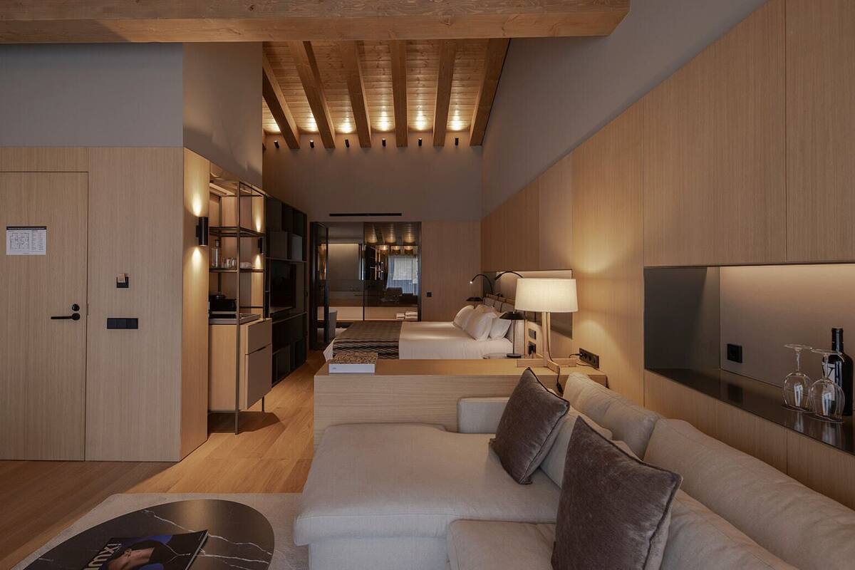 Une chambre d’hôtel moderne avec un plafond en bois, un canapé, un lit, une télévision et un mini-bar.