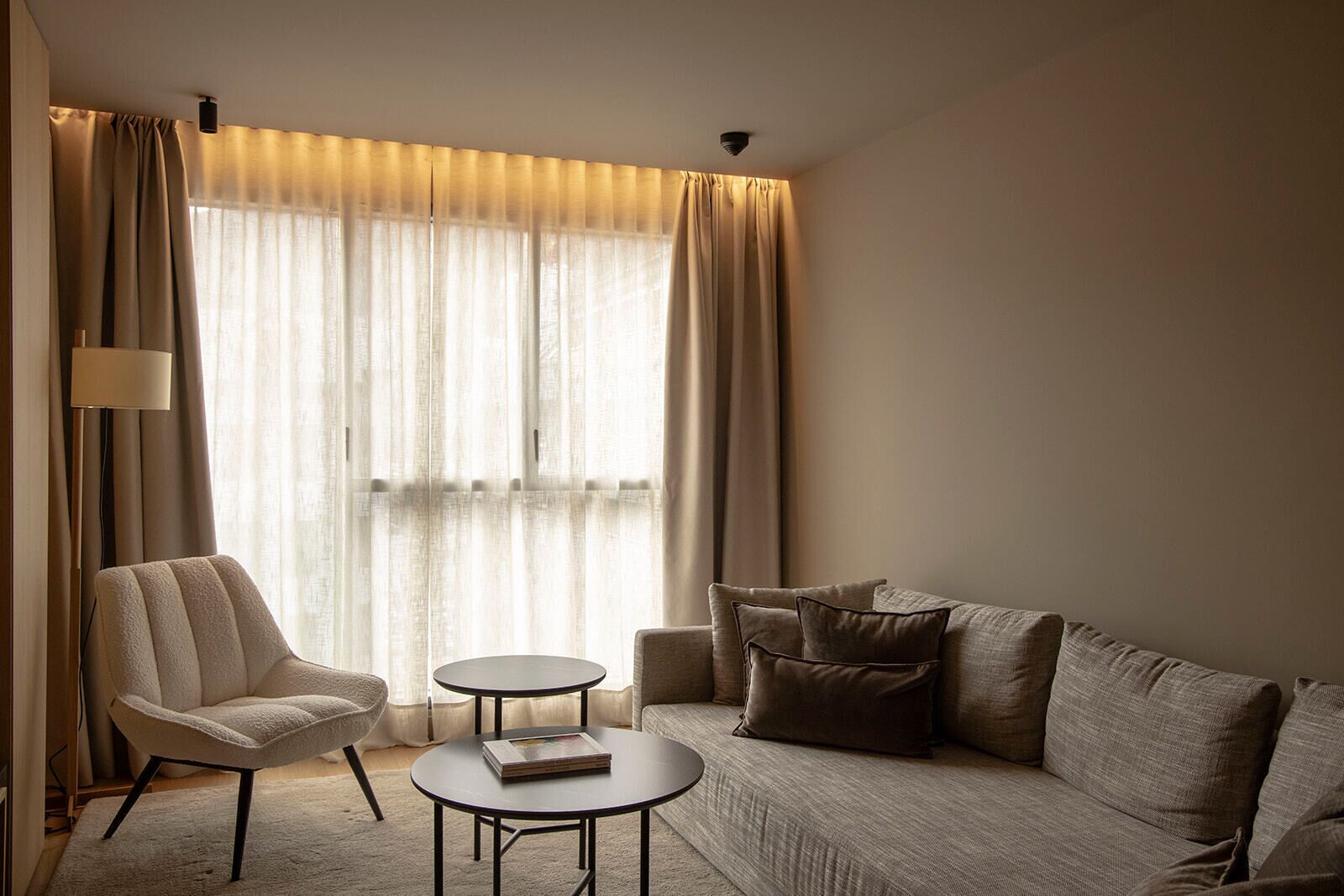 A modern hotel room with a sofa, armchair, and a small round table.