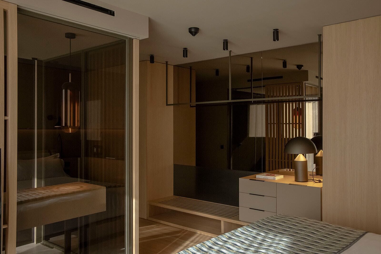 A modern bedroom with a glass wardrobe, a bedside table with a lamp, and a bed with a striped bedspread.