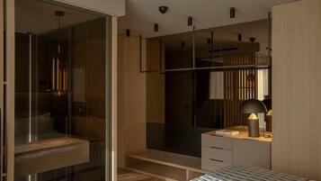 A modern bedroom with a glass wardrobe, a bedside table with a lamp, and a bed with a striped bedspread.