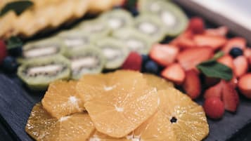 Una variedad de frutas frescas, como naranjas, kiwis y fresas, dispuestas sobre una tabla de pizarra oscura.