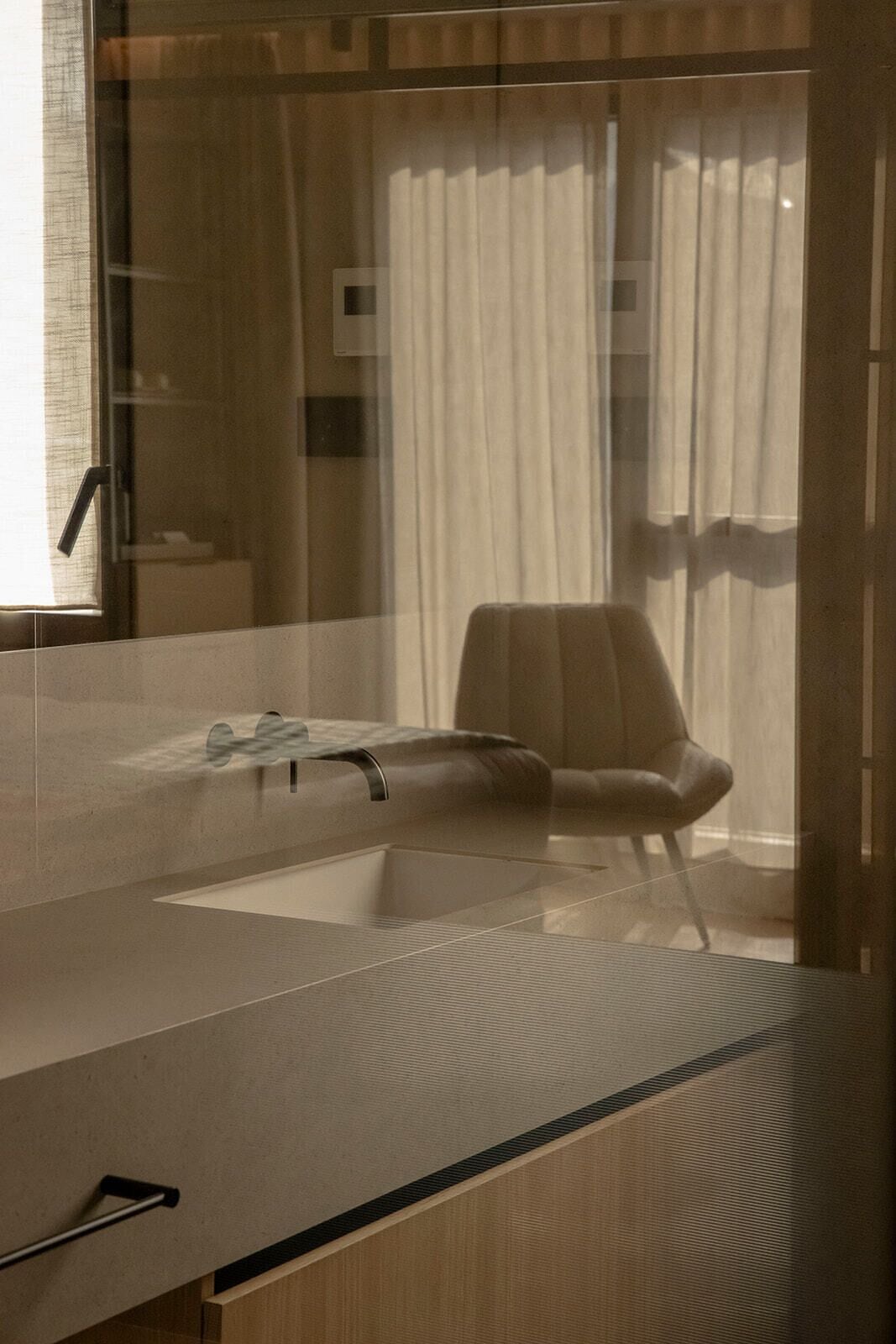 Un baño moderno con un espejo grande, un lavamanos y una silla.