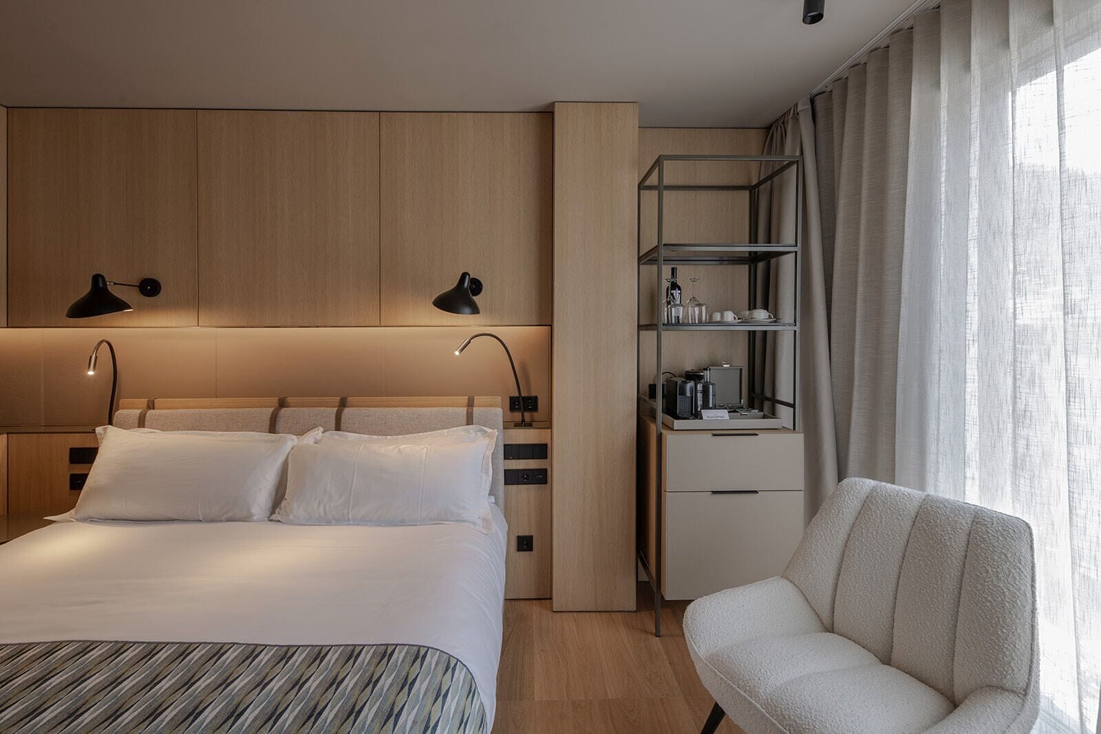 Una habitación de hotel moderna con una cama grande, lámparas de noche, un escritorio con una silla y una ventana con cortinas.