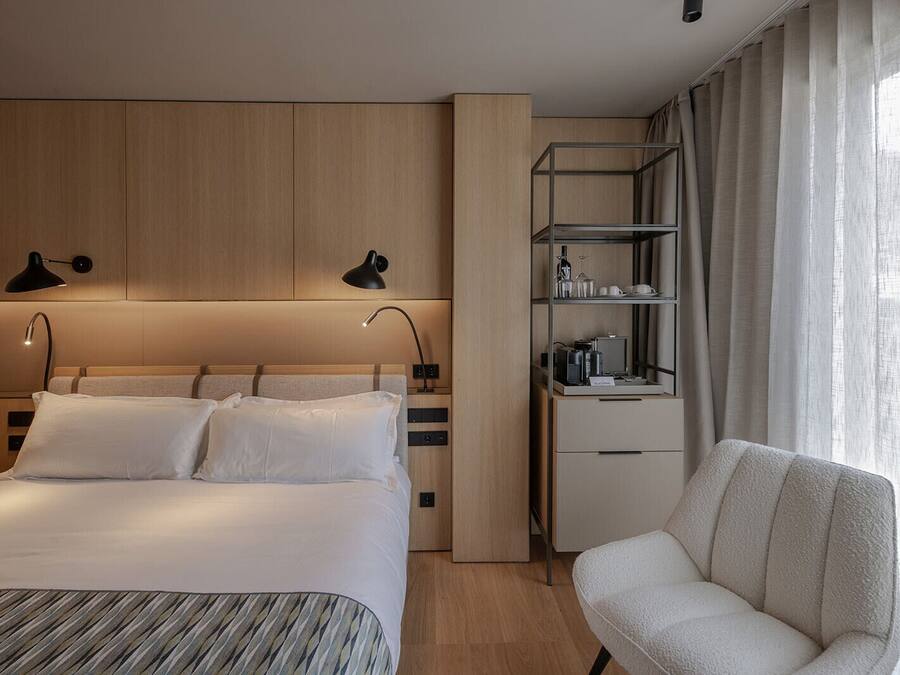 Ein modernes Hotelzimmer mit einem großen Bett, Nachttischlampen, einem Schreibtisch mit Stuhl und einem Fenster mit Vorhängen.