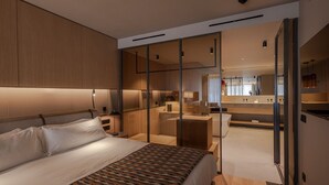 Een moderne hotelkamer met een groot bed, een aparte zithoek en een badkamer die zichtbaar is via een glazen wand.
