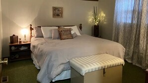 Un dormitorio ordenado con una cama grande, mesitas de noche, una mesita auxiliar, un reloj de pared y un cartel decorativo.