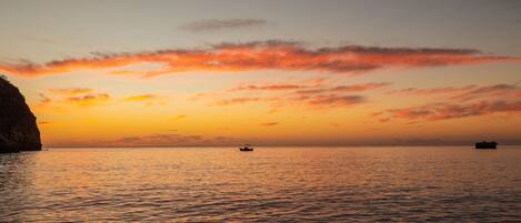 A sunset over a calm sea with a boat and a distant landmass.