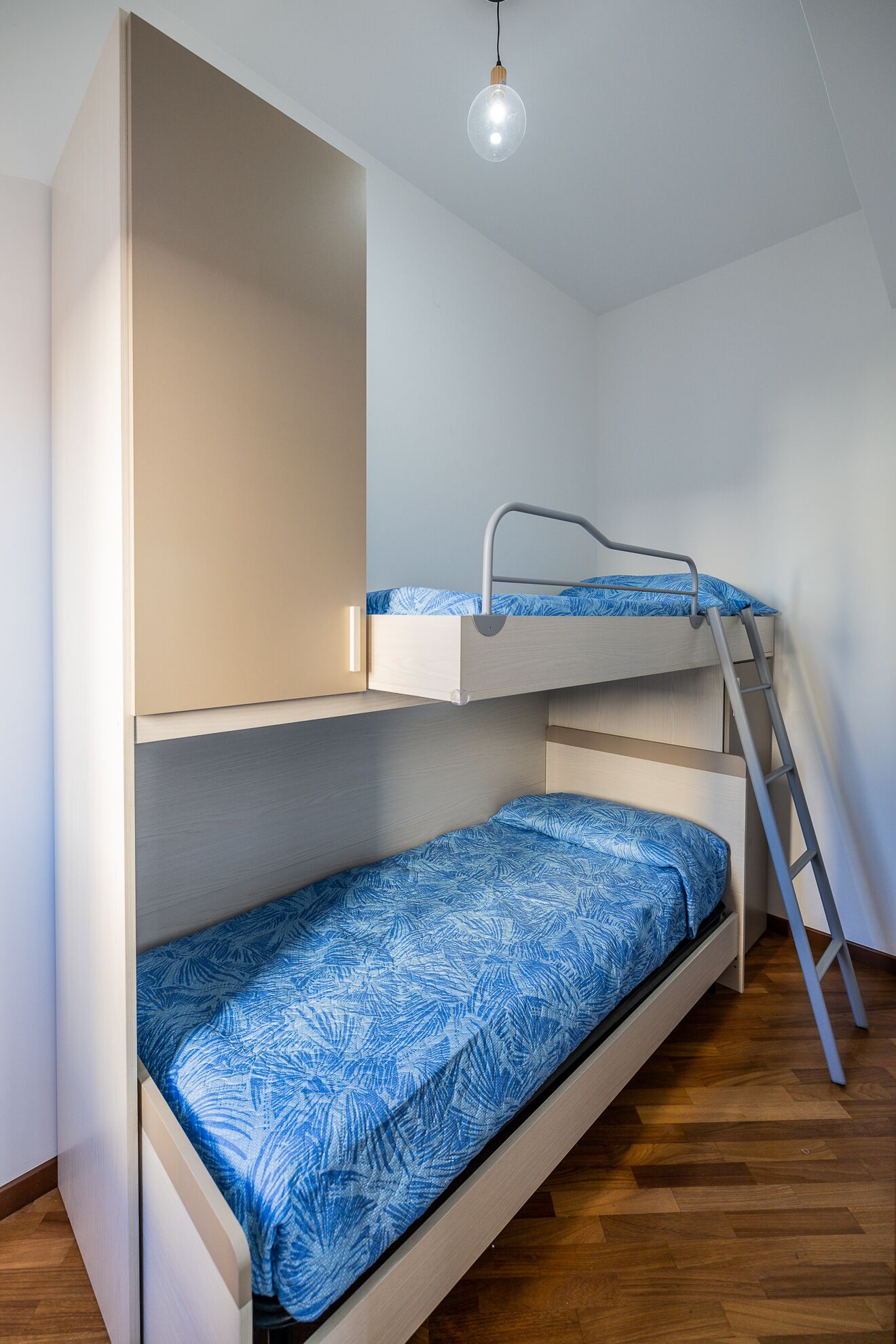 A bunk bed with a ladder, a light fixture, and a wooden floor.