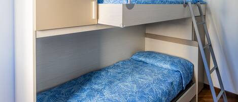 A bunk bed with a ladder, a light fixture, and a wooden floor.