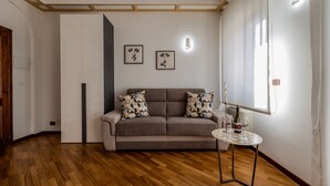 A modern living room with a sofa, two patterned cushions, a round table with two wine glasses, and a window with curtains. - I Barcaioli (Giardini Naxos)