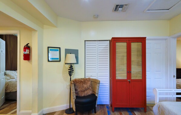 A hotel room with a bed, a red wardrobe, a white door, a framed certificate on the wall, and a fire extinguisher.