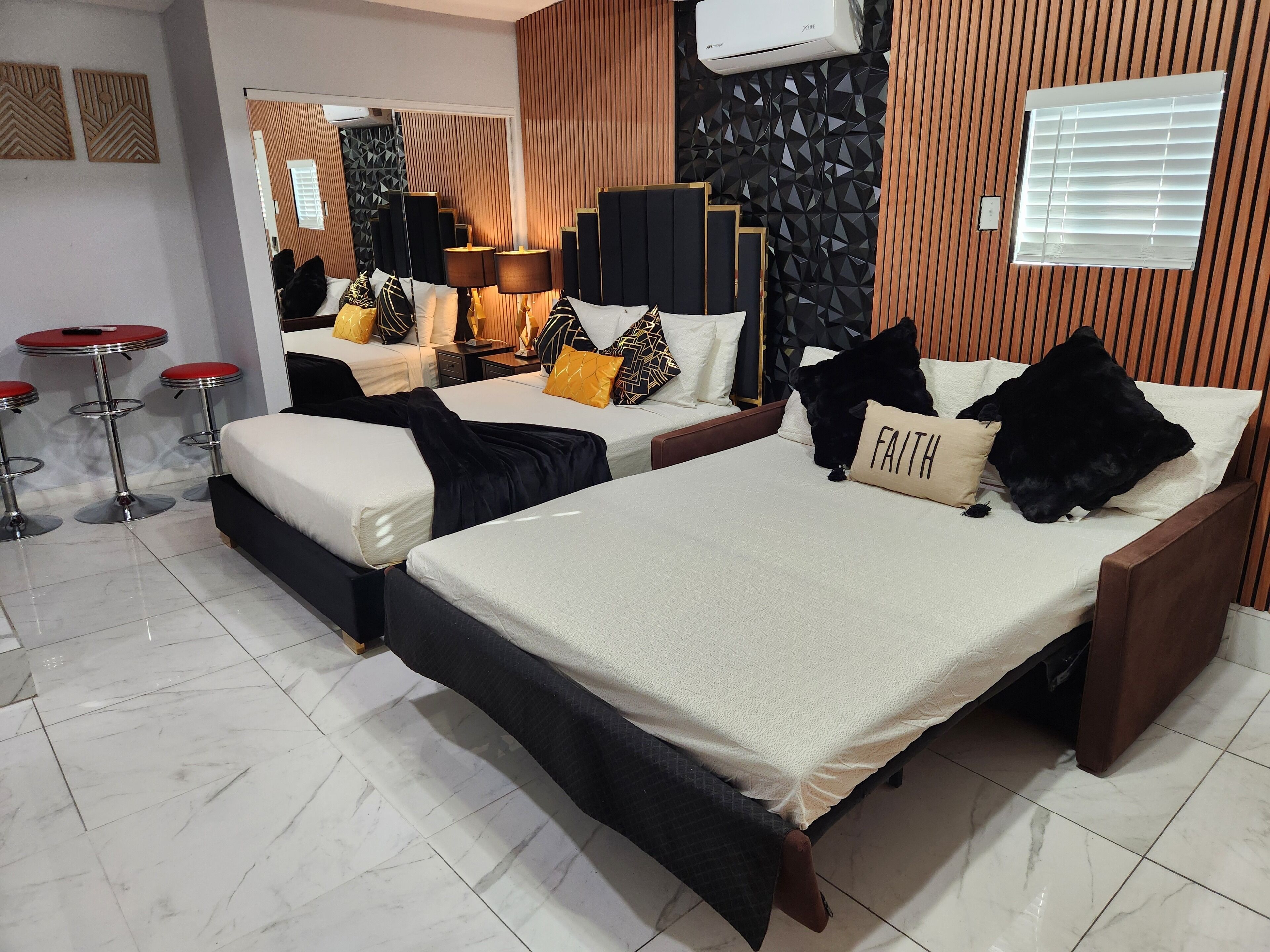Ein Hotelzimmer mit zwei Betten, einer Sitzecke mit einer roten Bar und einem modernen Design mit geometrischen Wandmustern.