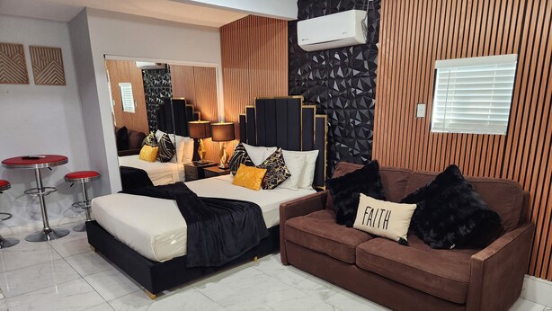 Un dormitorio moderno con una cama, un sofá marrón y un taburete rojo.
