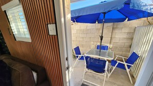 Un patio con una mesa, sillas azules, una sombrilla azul y una pared de madera con una ventana.