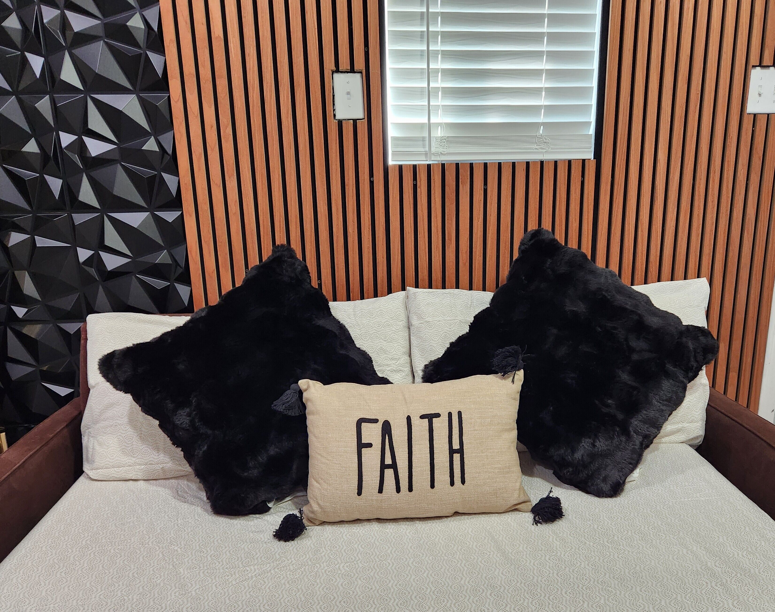 A bed with two black pillows and a beige pillow with the word "FAITH" on it.