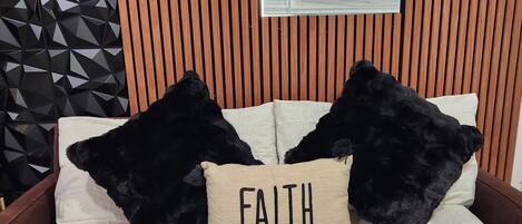 A bed with two black pillows and a beige pillow with the word "FAITH" on it.