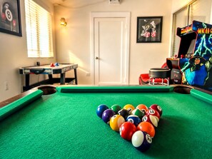 A pool table with balls in the center, a table tennis table, and arcade games in the background. - Family Largue House: Slide, Game Room & Jacuzzi
(Las Vegas)