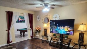 Ein Wohnzimmer mit Flachbildfernseher, Deckenventilator, Billardtisch und einer Couch.