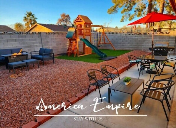 Un jardin avec un espace de jeux, un barbecue et un coin salon extérieur.