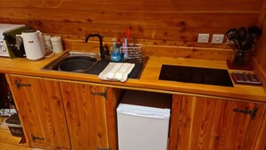 A compact kitchen with wooden cabinets, a sink, a small refrigerator, and various kitchen appliances.